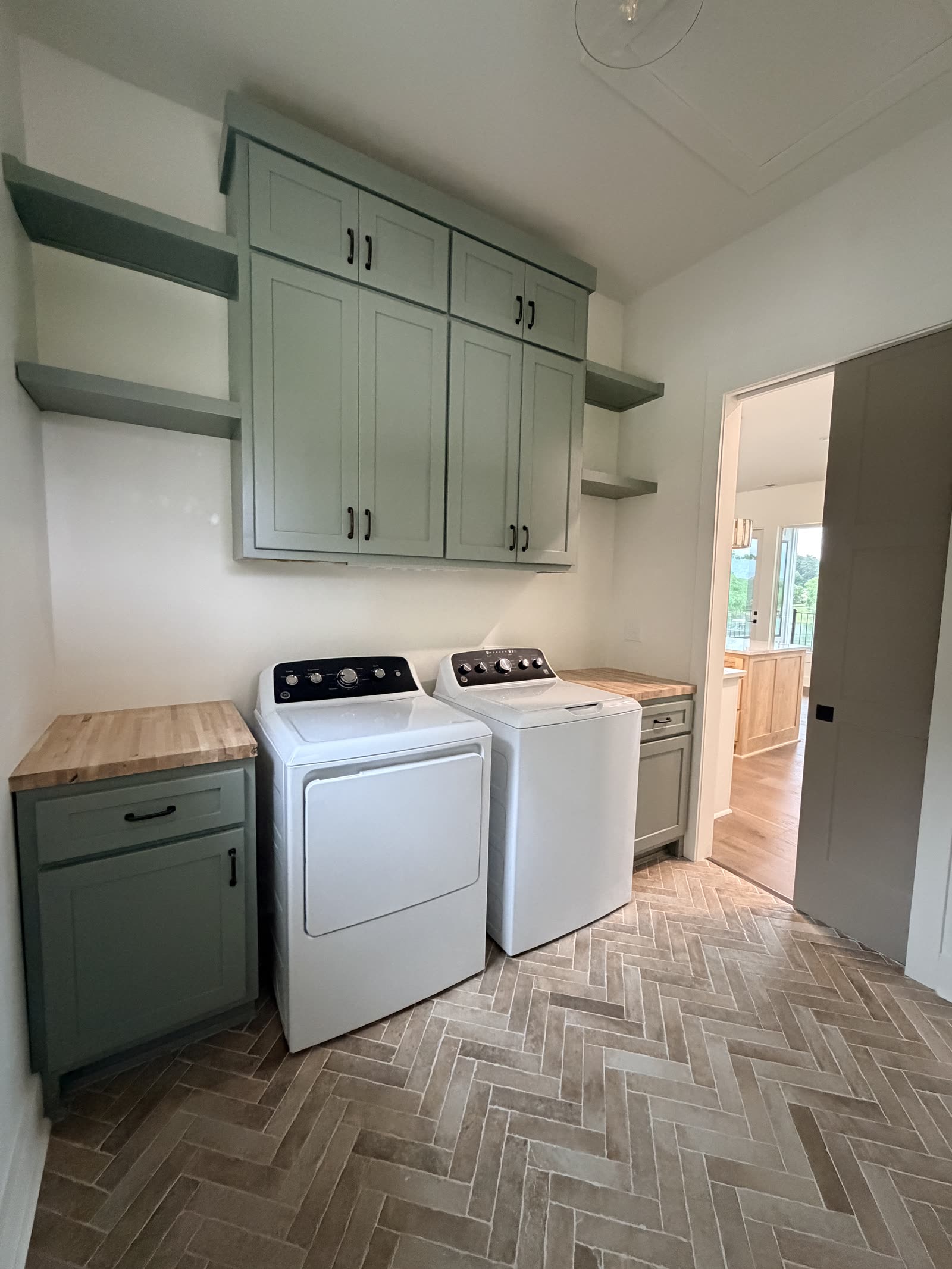 Laundry room with sage cabinets and herringbone tile